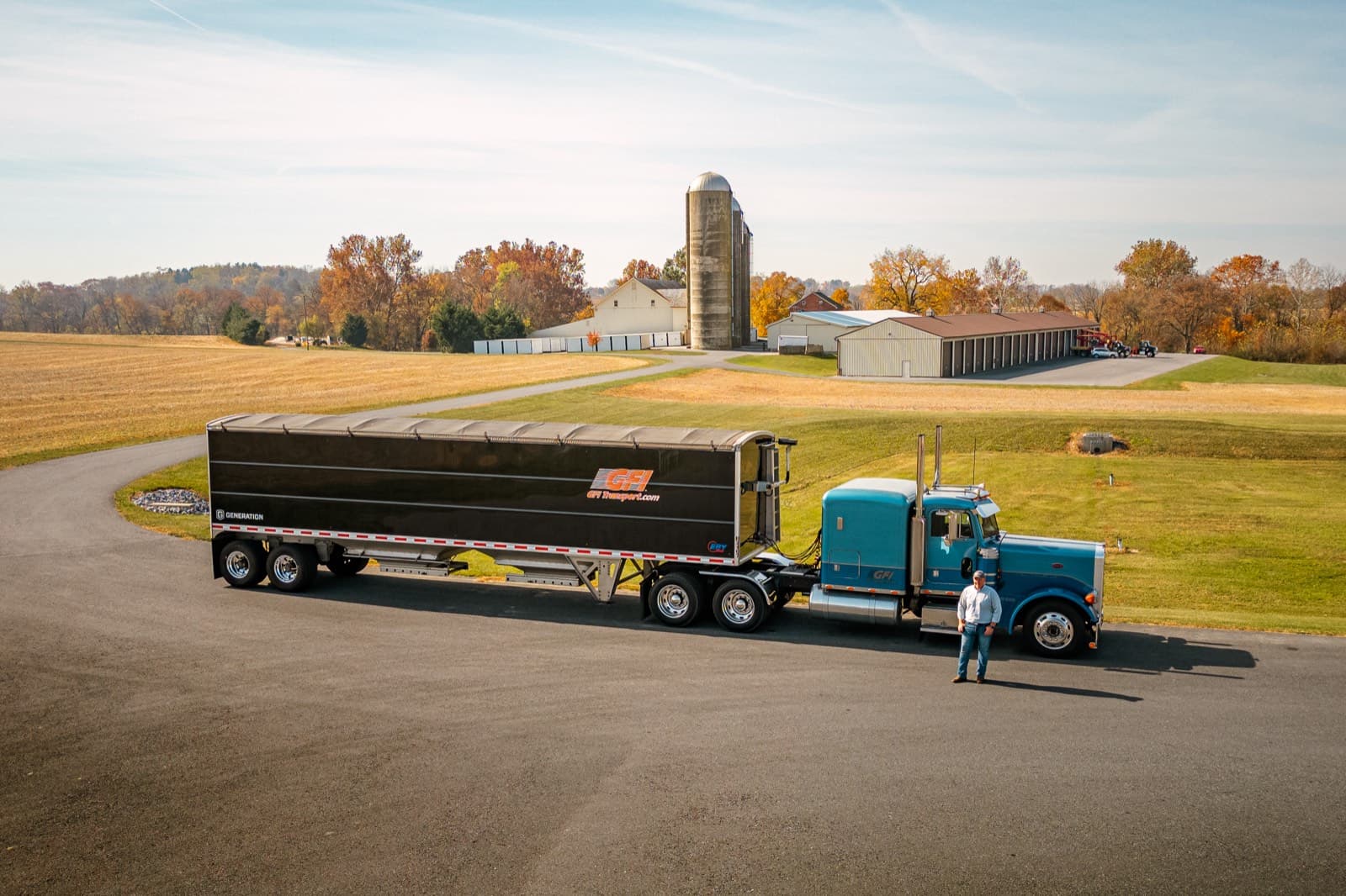 An owner operator standing beside his tractor and hopper trailer on a farm lane