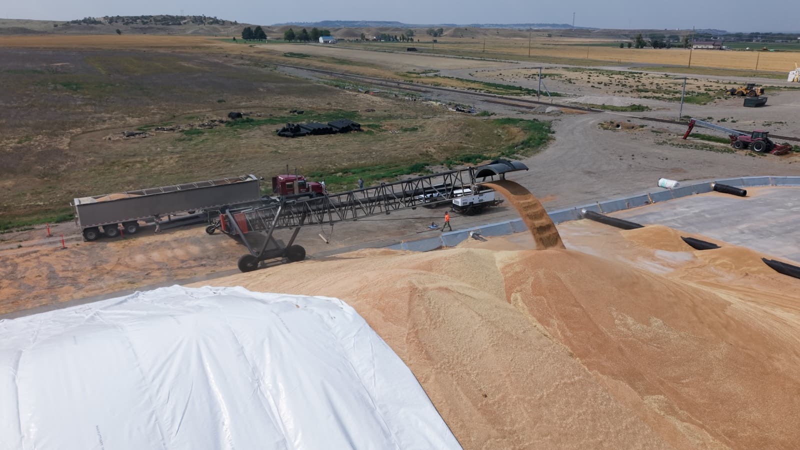 Grain augering onto the pile at an origin facility as a truck unloads alongside